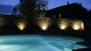 A swimming pool with a stone wall and a house in the background. - Relais Corte Guastalla (Sona)