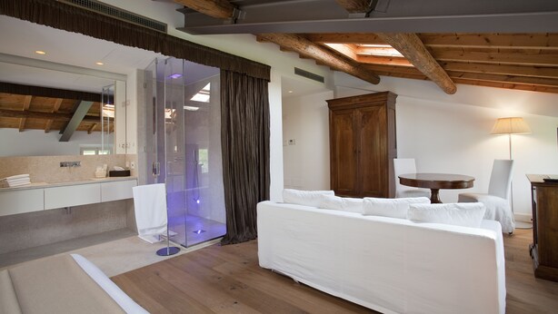 A modern room with a wooden ceiling, a glass shower, a white sofa, and a round table. - Relais Corte Guastalla (Sona)
