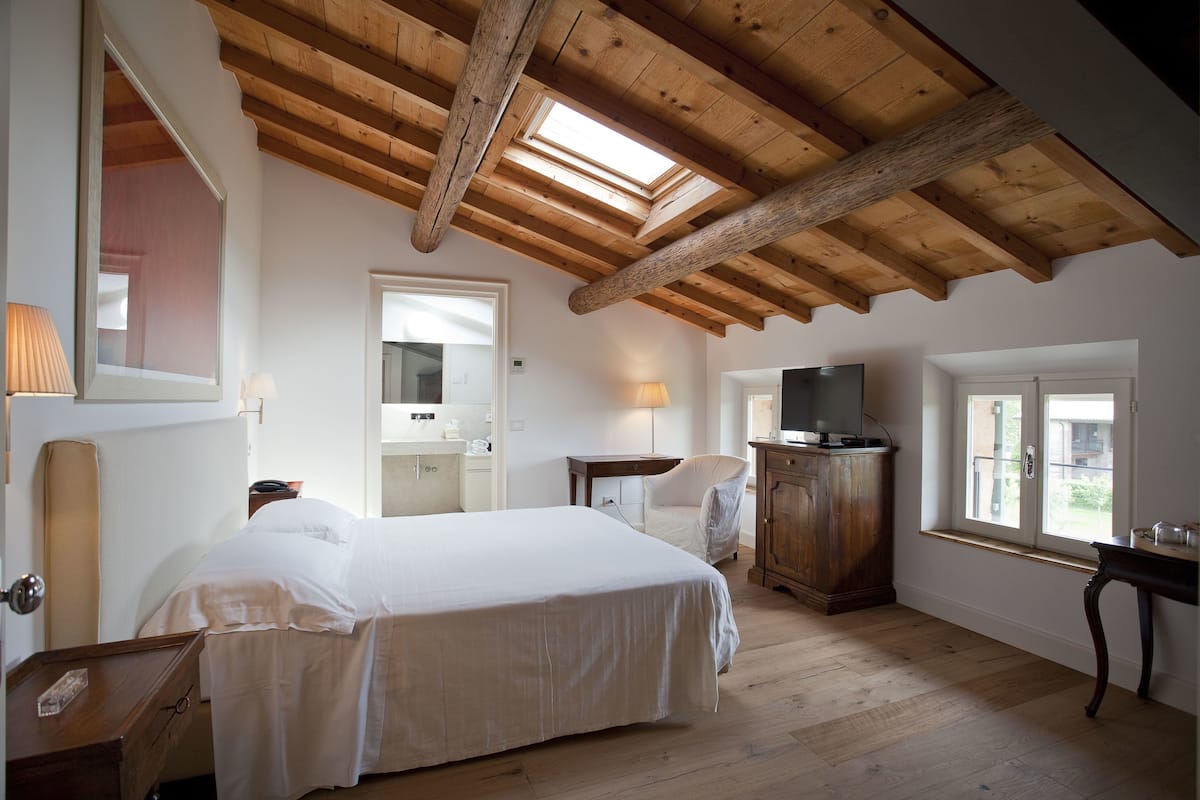 A bedroom with a wooden ceiling, a bed, a TV, and a window.