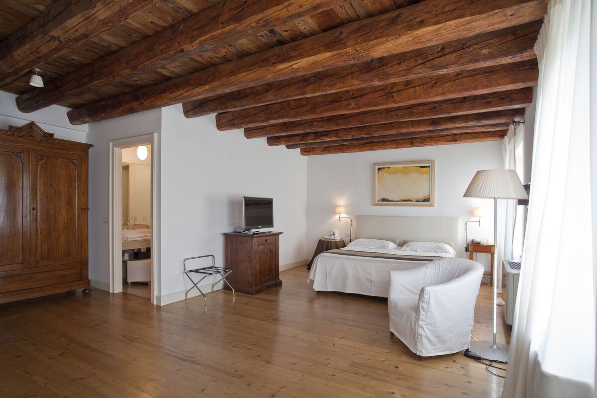A bedroom with wooden beams, a bed, a TV, a bedside table, and a lamp.