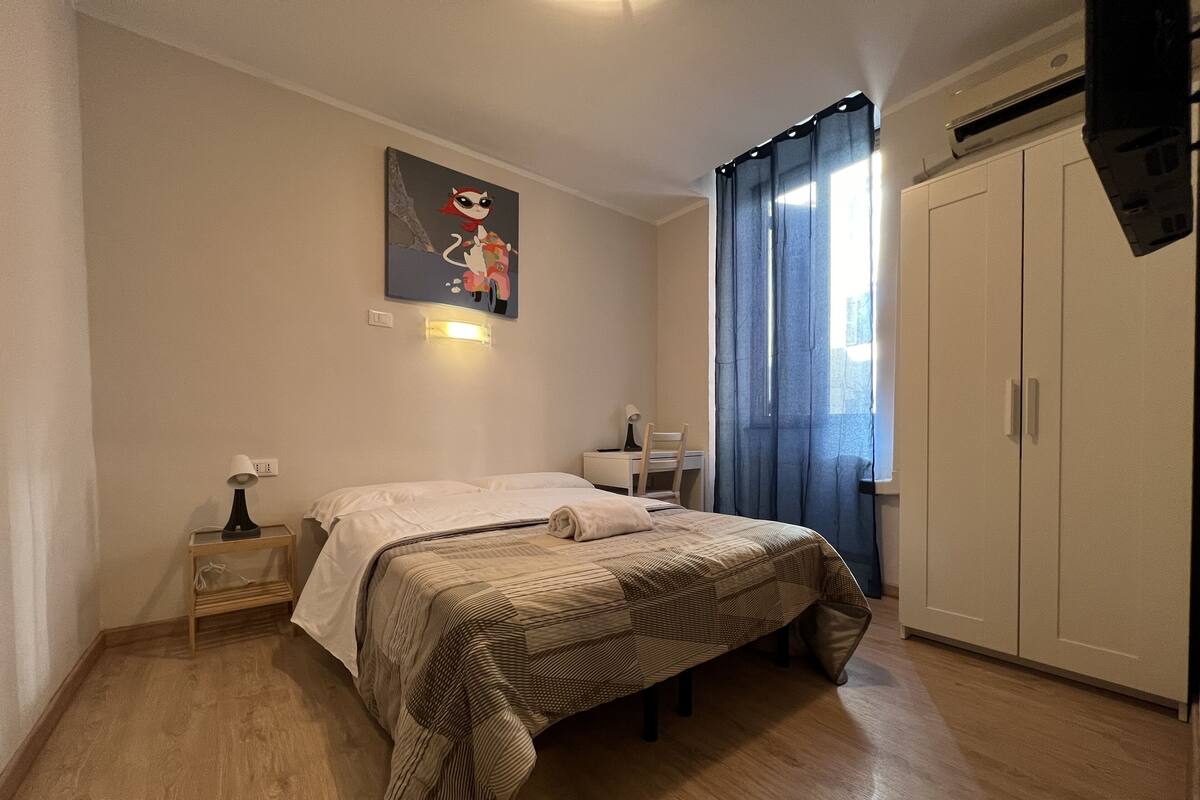 A bedroom with a bed, a desk, a chair, a wardrobe, and a painting on the wall.