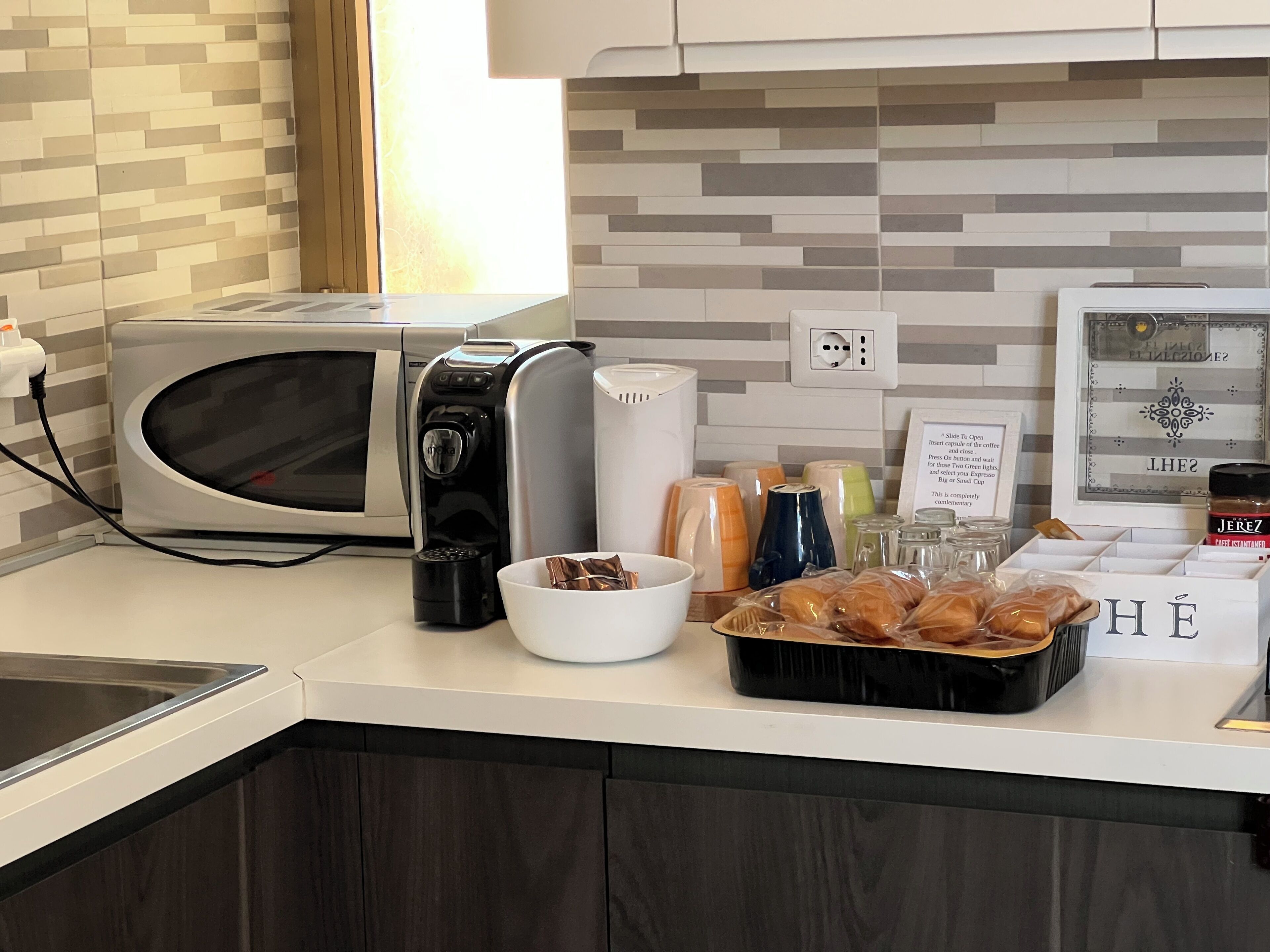 Une cuisine équipée d’un four à micro-ondes, d’une machine à café et de divers ustensiles de cuisine disposés sur le plan de travail.