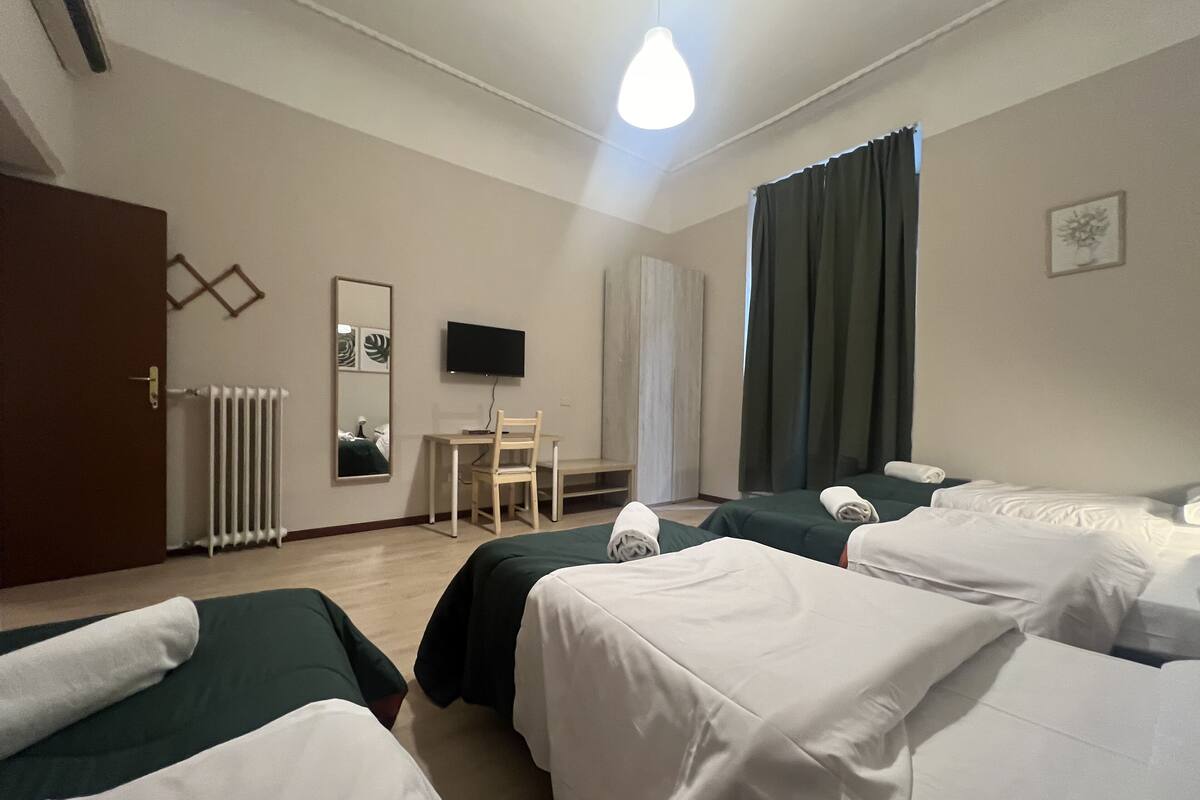 A hotel room with two beds, a desk, a chair, a television, and a window with curtains.