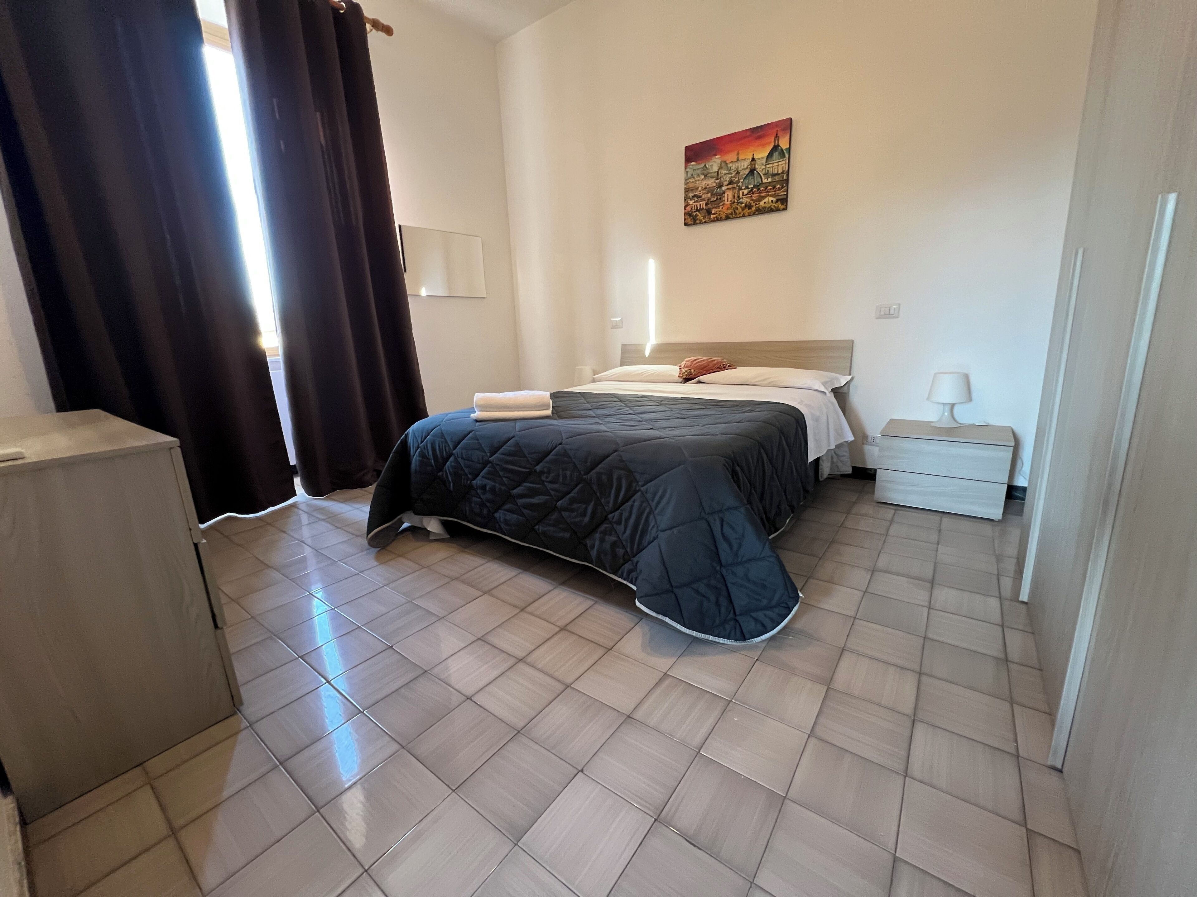 Un dormitorio ordenado con cama, mesita de noche, lámpara y un cuadro en la pared.