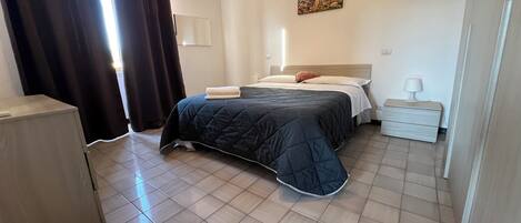 Un dormitorio ordenado con cama, mesita de noche, lámpara y un cuadro en la pared.