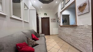 A modern living room with a grey sofa, red cushions, a stone-textured wall, and a wooden reception desk. - Freedom Traveller Hostel (Rome)