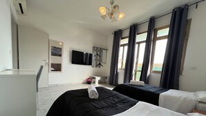 A hotel room with two beds, a desk, a chair, a TV, and a window with curtains. - Freedom Traveller Hostel (Rome)