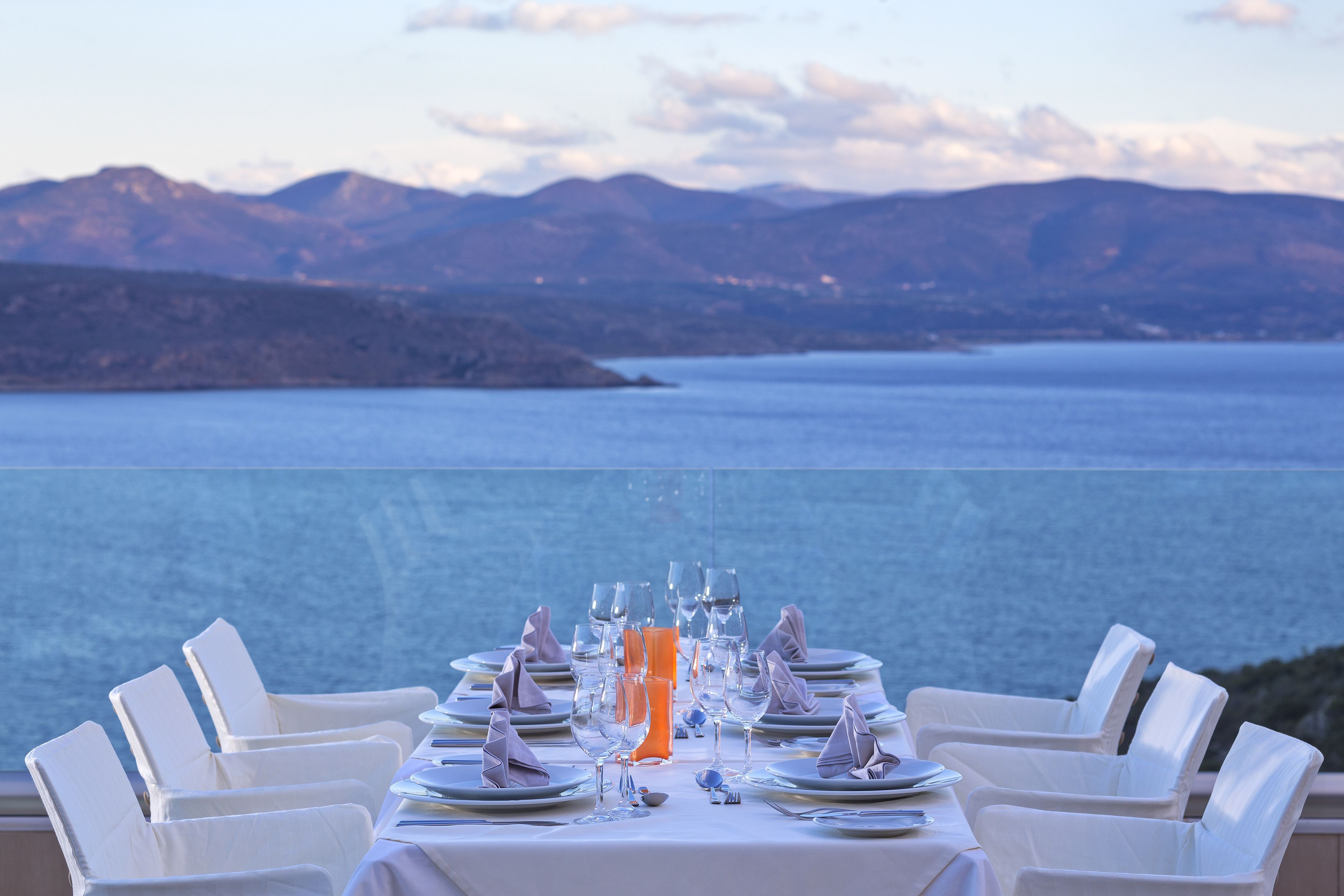 A table set for a meal with a view of a large body of water and mountains in the background.