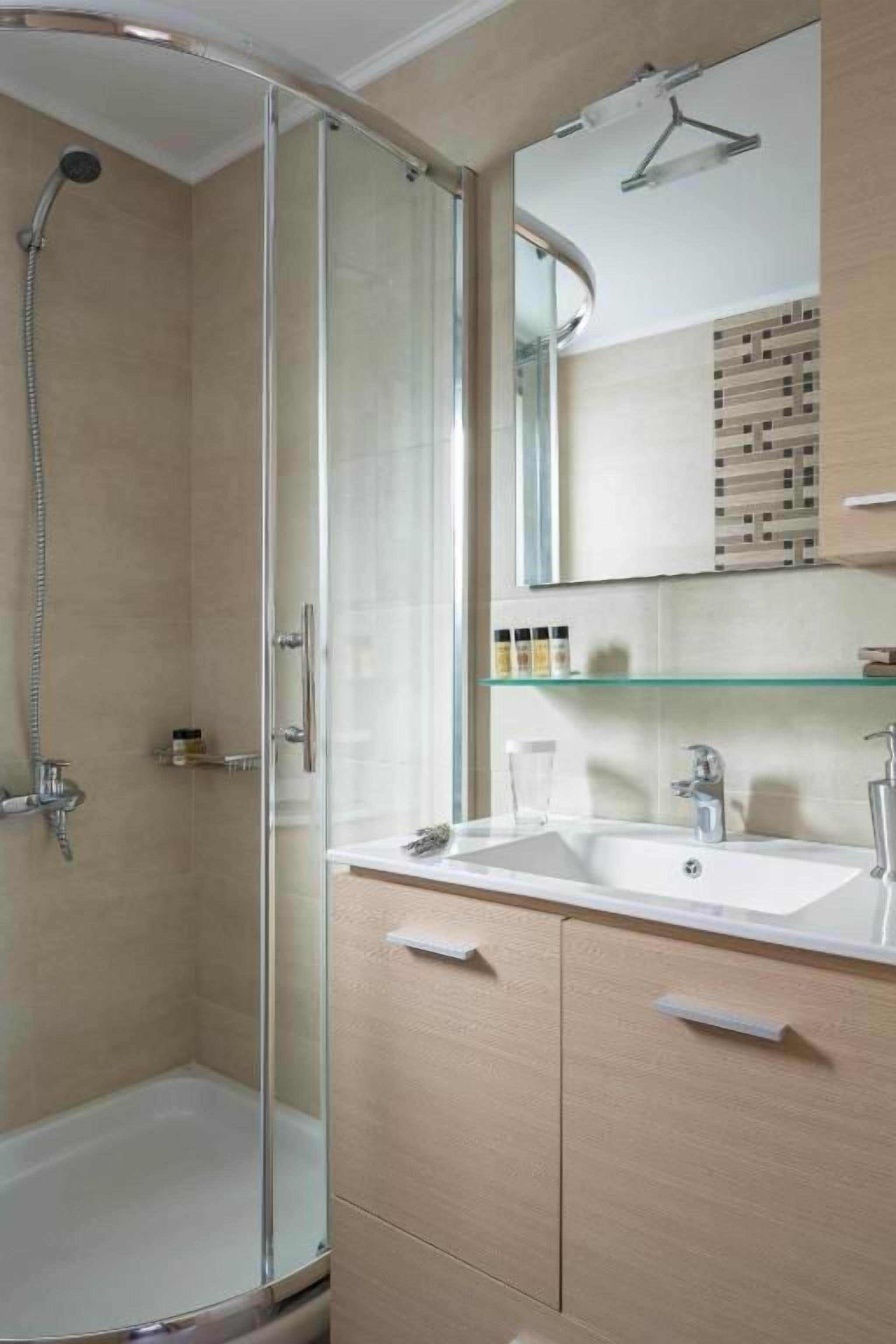 A bathroom with a glass shower enclosure, a sink with a mirror above, and a cabinet below.