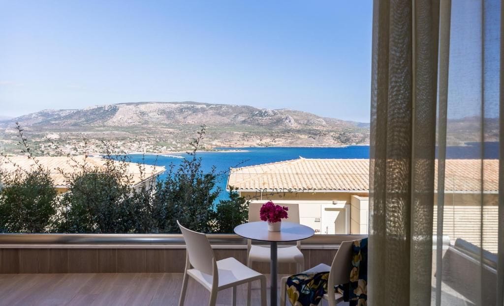 A balcony with a table and chairs overlooking a coastal landscape.