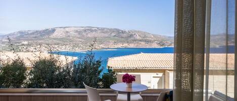 A balcony with a table and chairs overlooking a coastal landscape.