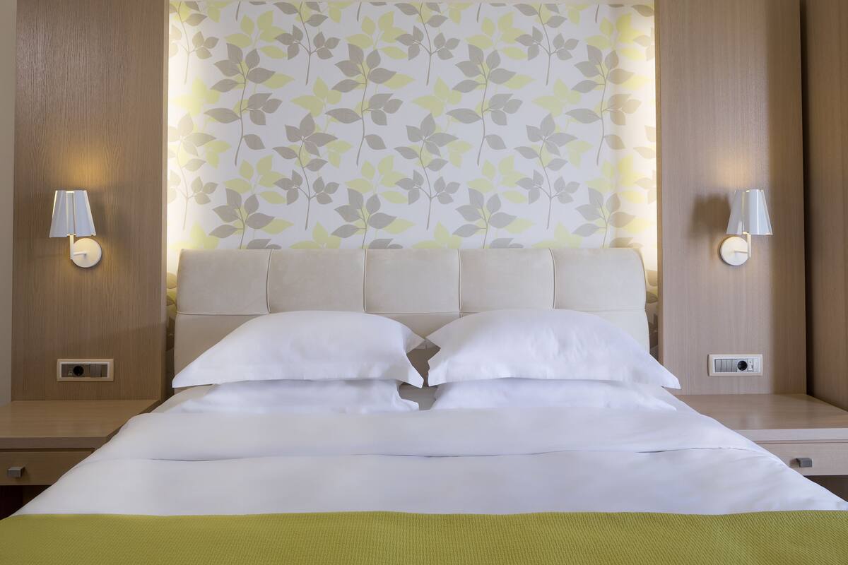 A neatly made bed with white linens, a green throw blanket, and two wall-mounted lamps on either side.
