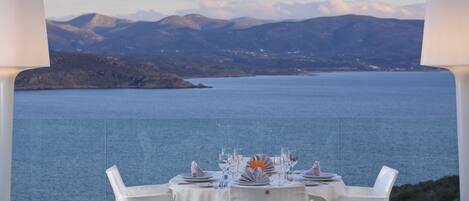 A table set for dining with a view of a calm sea and mountains in the background.