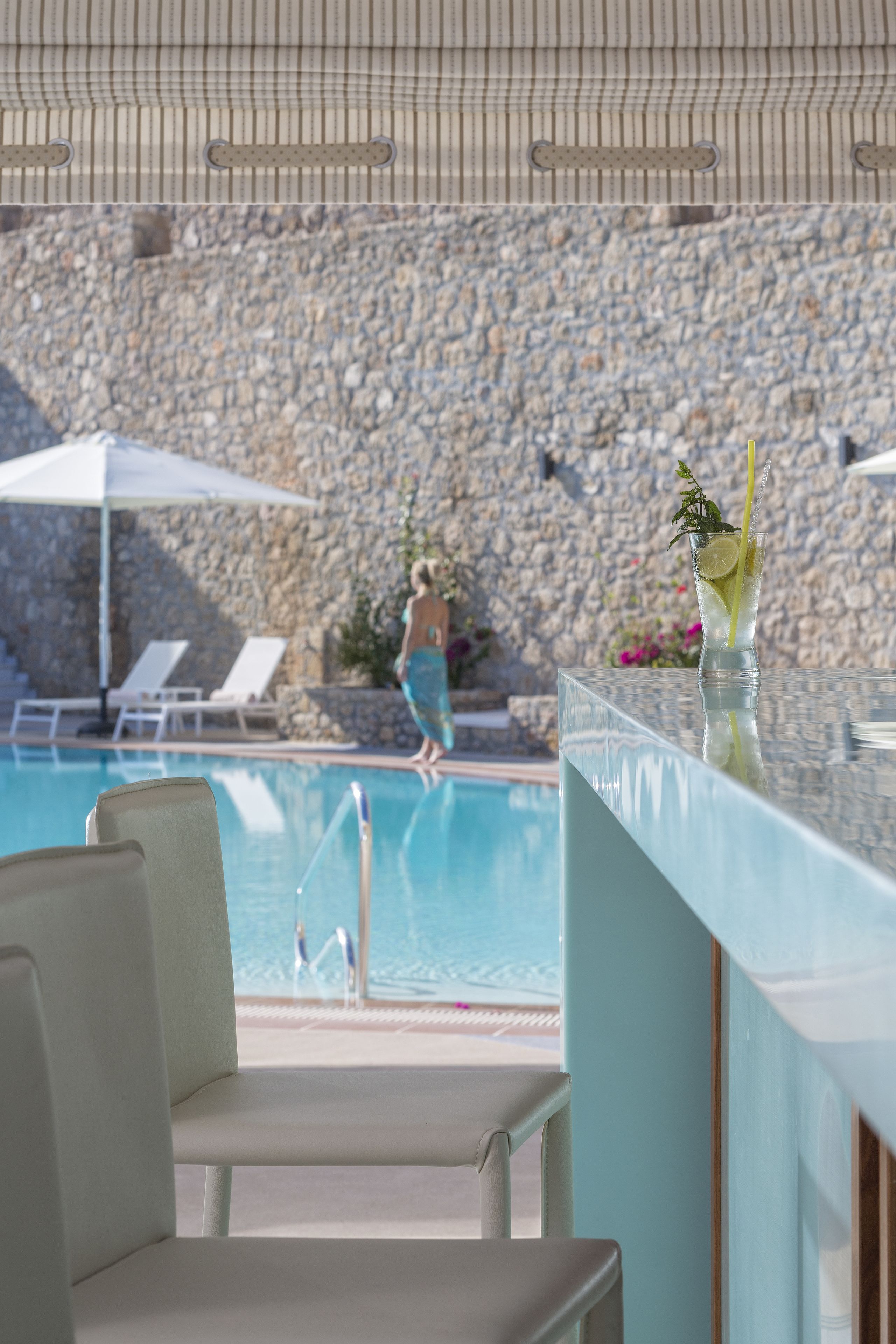 A poolside area with lounge chairs, a bar, and a stone wall in the background.