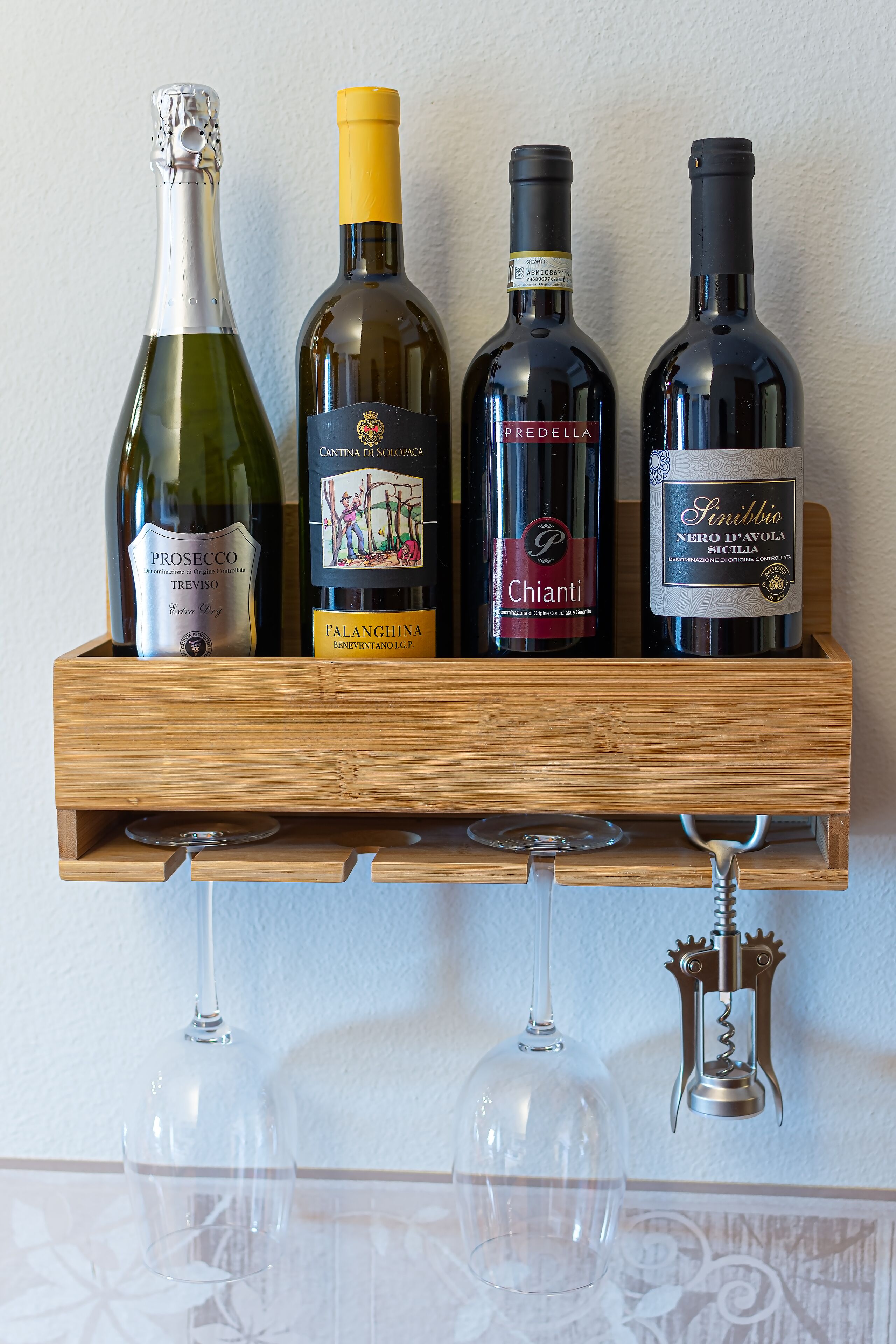 A wooden wine rack holding four bottles of wine and two wine glasses.