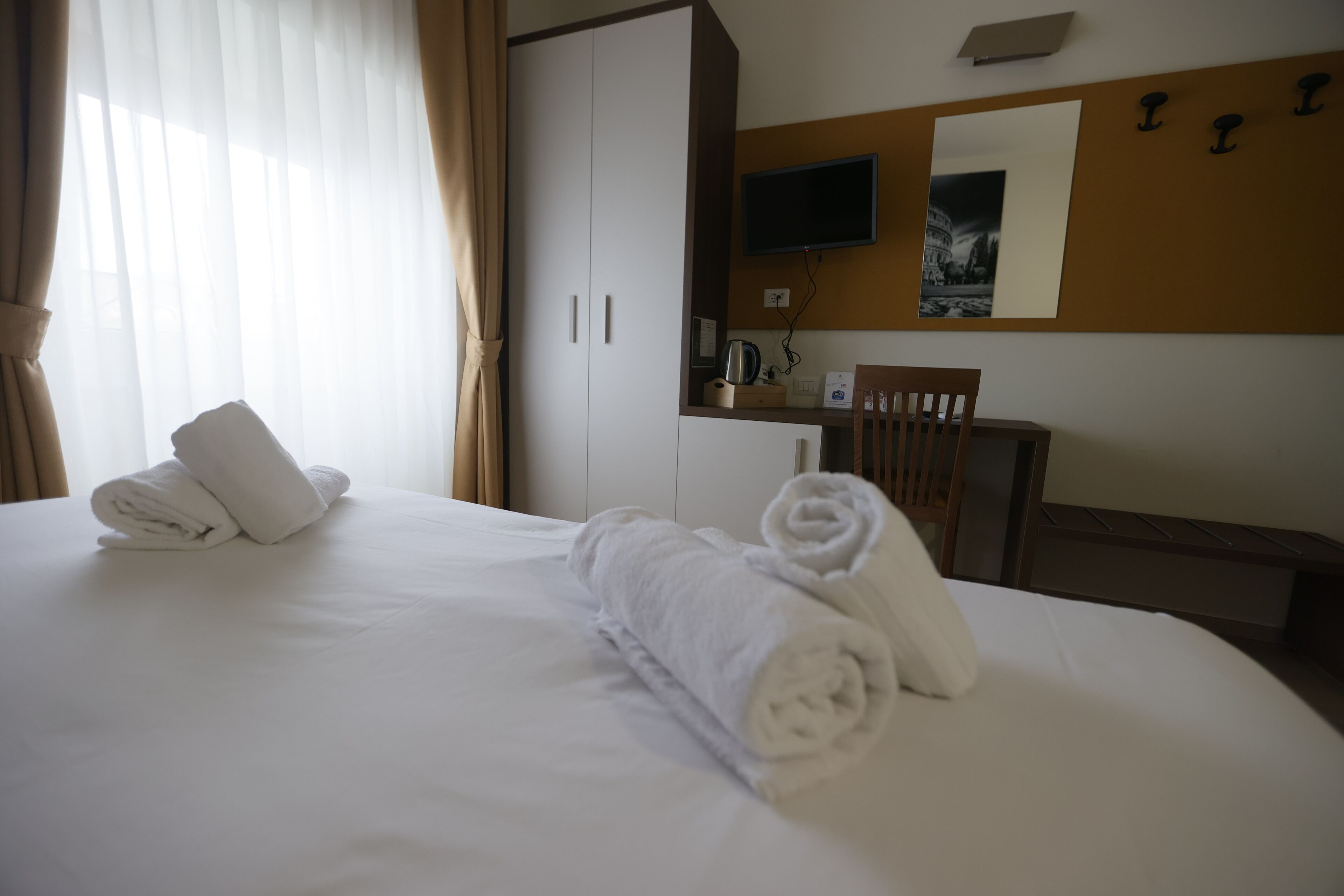 A hotel room with a neatly made bed, a desk with a chair, a television, and a mirror on the wall.