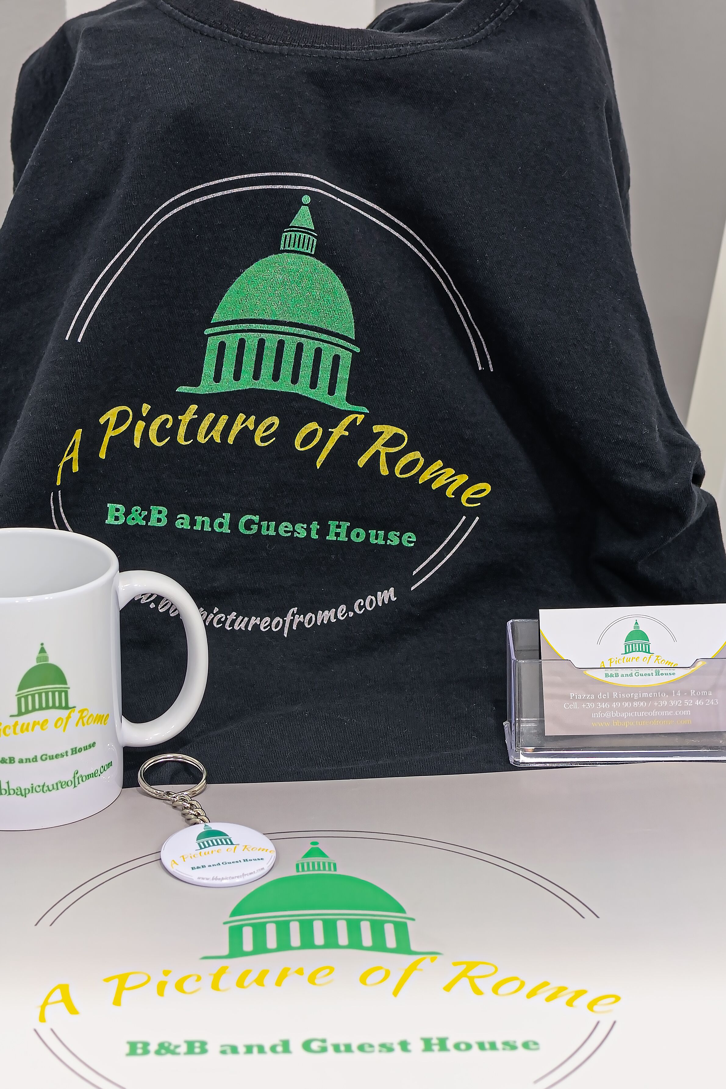 Una camiseta negra con una cúpula verde y texto, una taza blanca, un CD y una tarjeta de presentación.