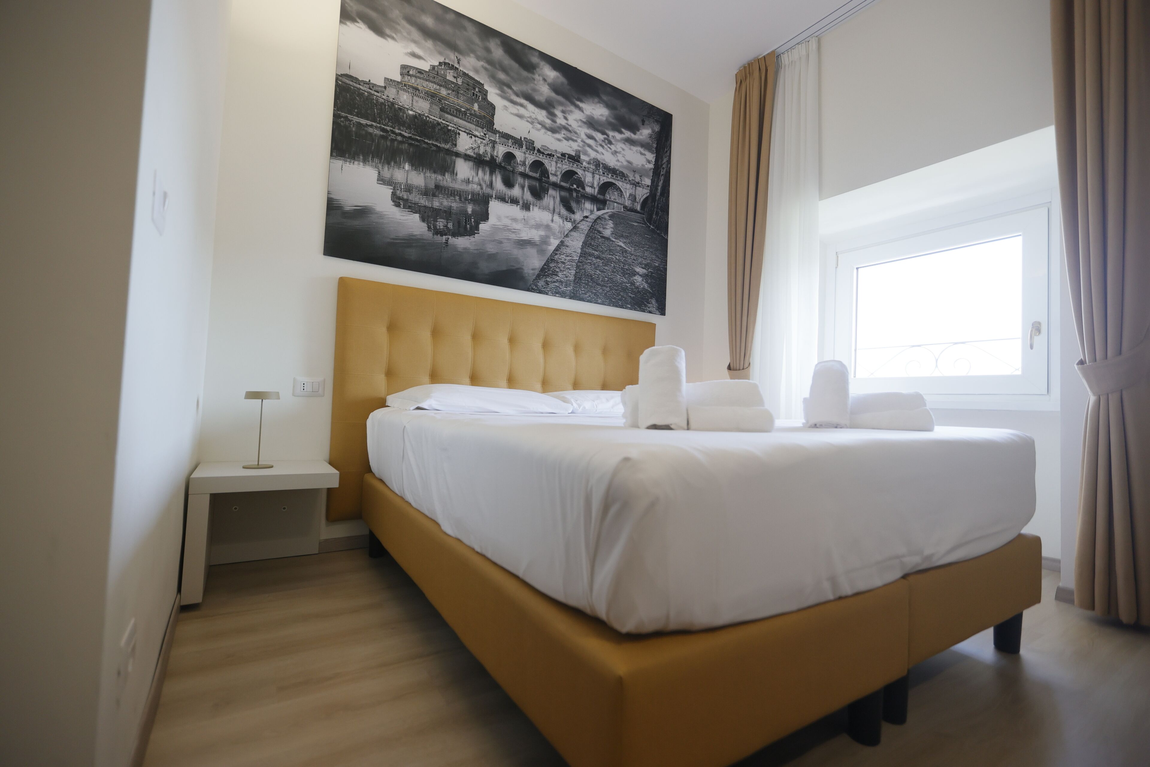 Una habitación de hotel con una cama grande, una mesita de noche, una lámpara y una ventana con cortinas.