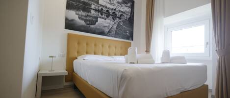 Una habitación de hotel con una cama grande, una mesita de noche, una lámpara y una ventana con cortinas.