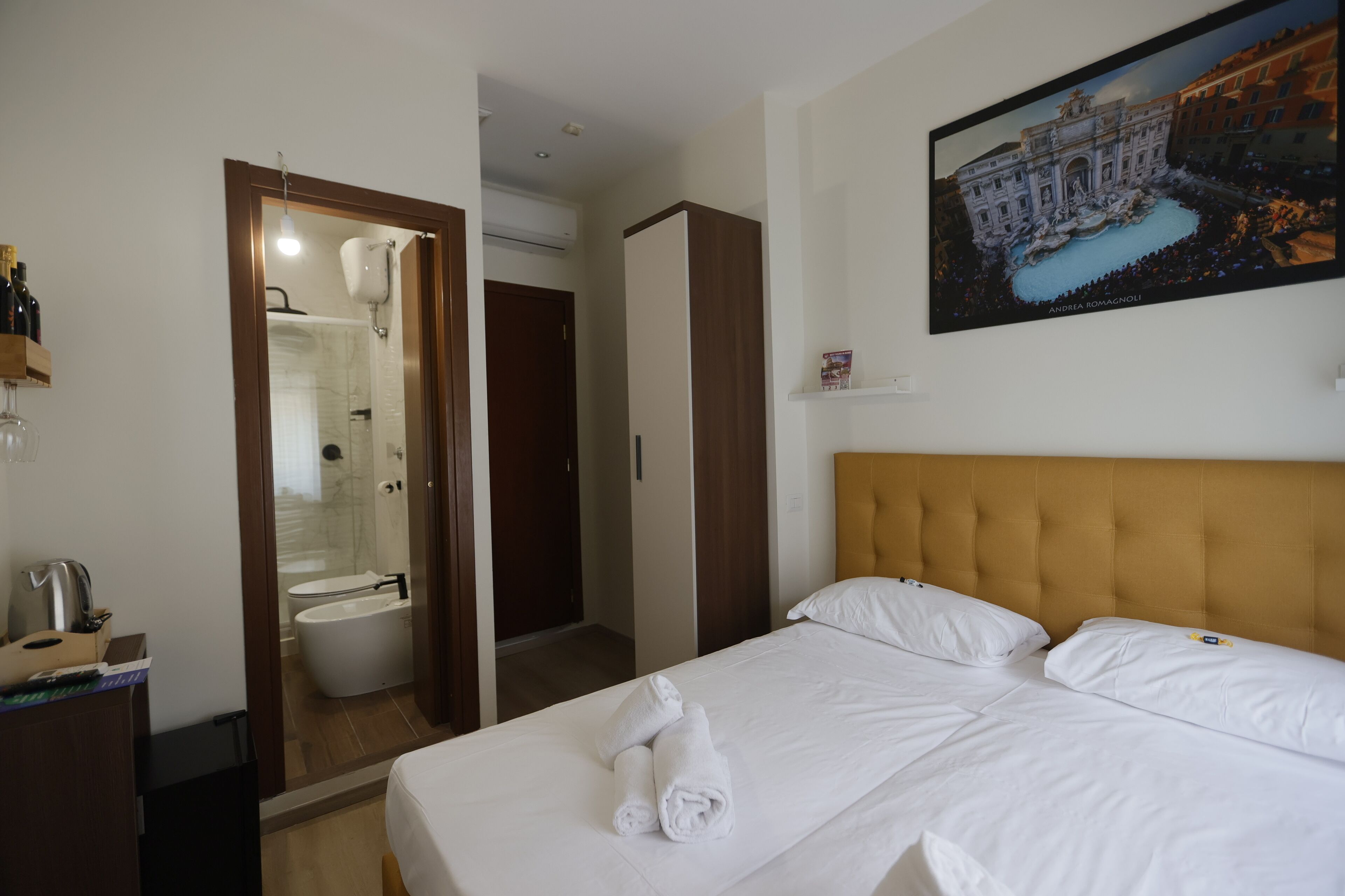 A hotel room with a bed, a painting of St. Peter's Basilica, a bathroom with a shower, and a minibar.