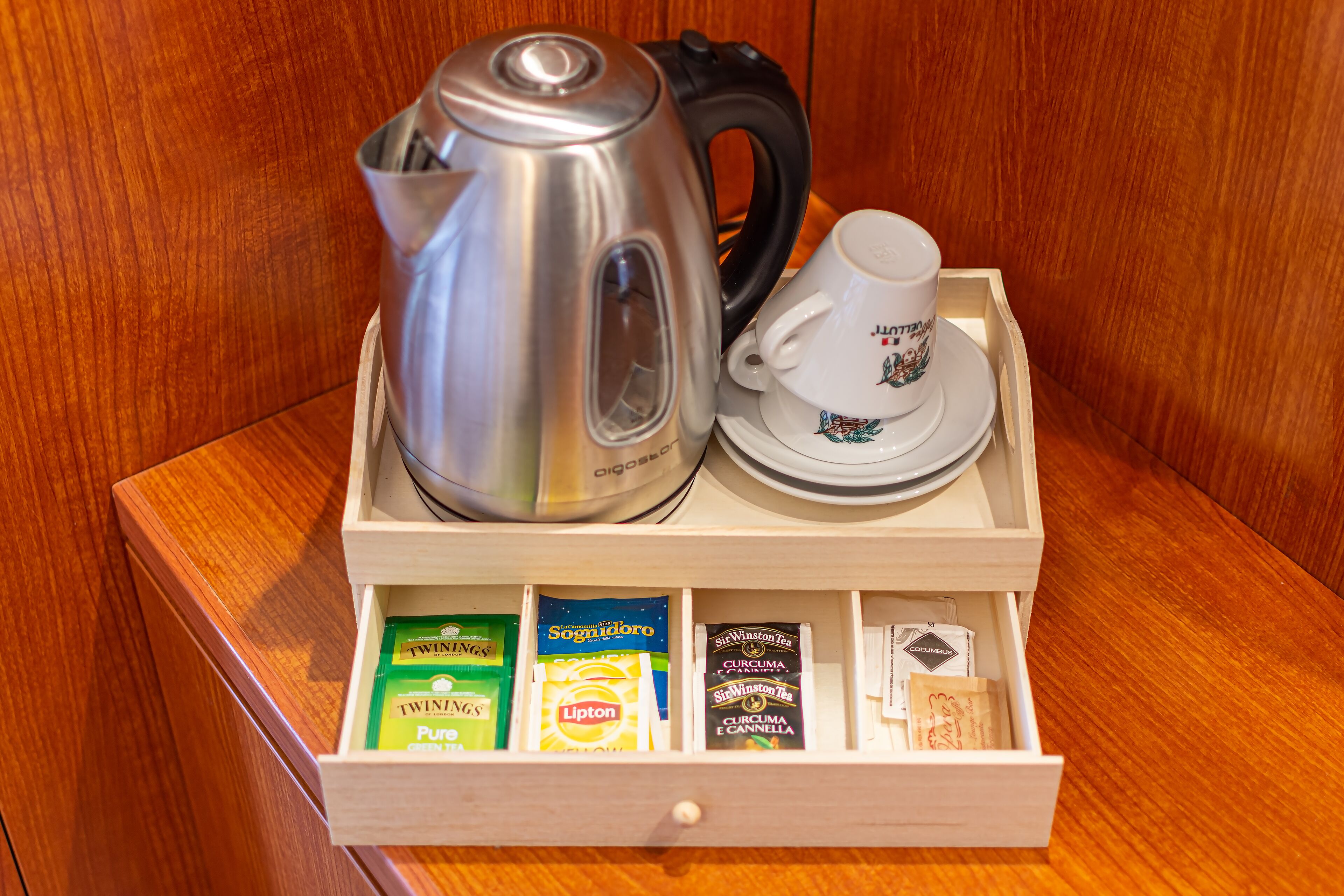 Un plateau en bois avec une bouilloire, une tasse et un tiroir contenant des sachets de thé.