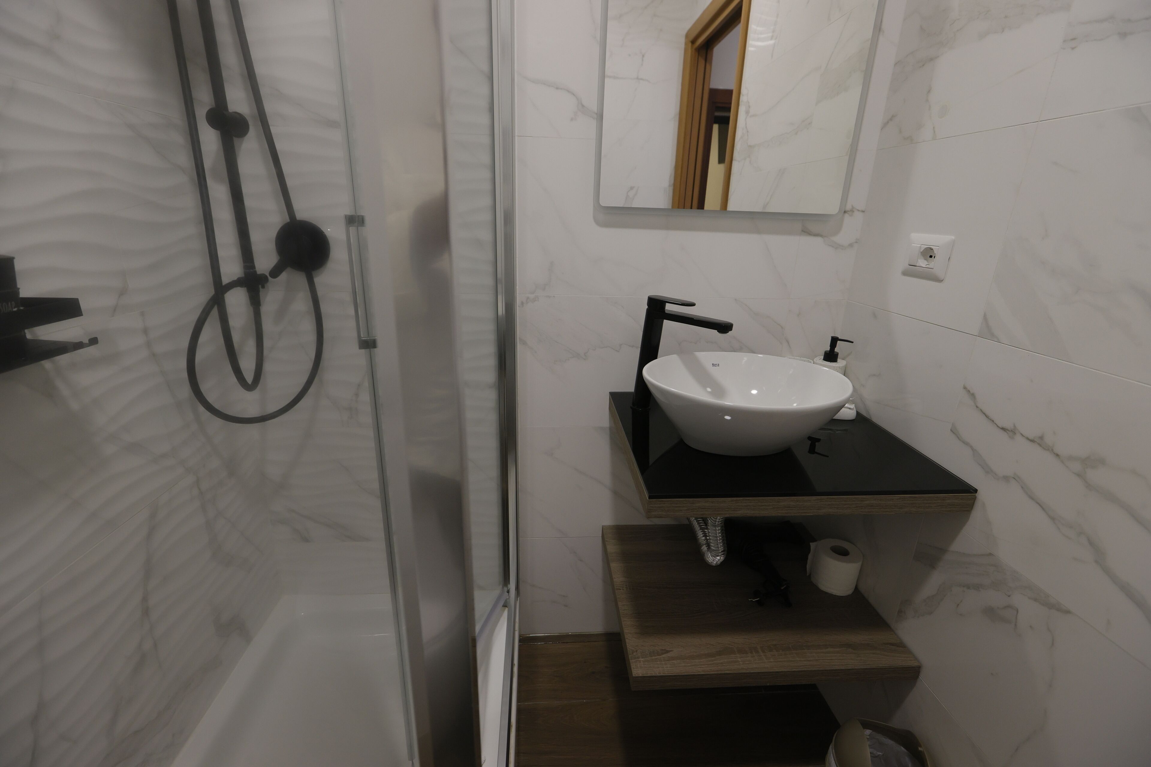 A modern bathroom with a white sink, black faucet, and a wooden vanity.