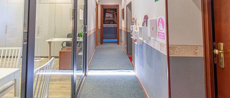A hotel corridor with a carpeted floor, a wooden door on the right, and a glass partition on the left.