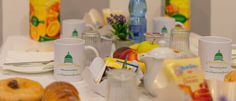 A breakfast table with various food items, a water bottle, and branded coffee mugs.