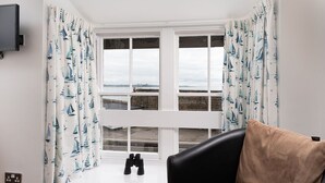 A room with a large window, curtains with a sailboat pattern, a black leather chair, and a pair of binoculars on the windowsill. - Dolphin Tavern (Penzance)