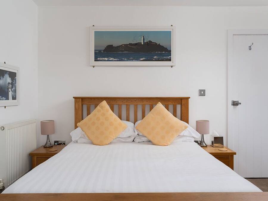 Una cama bien hecha con dos almohadas, un cabecero de madera, un cuadro en la pared y una puerta blanca.