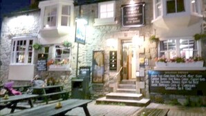 A stone building with a signboard, outdoor seating, and a staircase leading to the entrance. - Dolphin Tavern (Penzance)