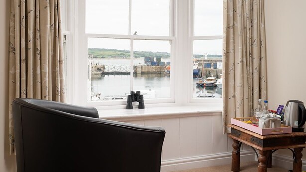 A room with a large window overlooking a harbor, a black chair, and a wooden table with a tray of items. - Dolphin Tavern (Penzance)
