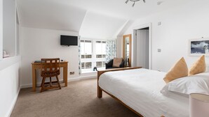 A bedroom with a bed, a desk, a chair, a TV, and a window with curtains. - Dolphin Tavern (Penzance)