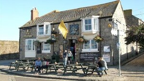 A stone building with a signboard, outdoor seating, and a flag. - Dolphin Tavern (Penzance)