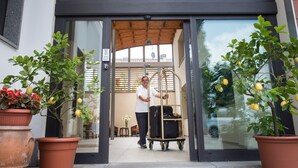 A man pushing a luggage cart through a glass door into a building with a wooden ceiling and potted lemon trees. - Hotel La Villetta (Calenzano)
