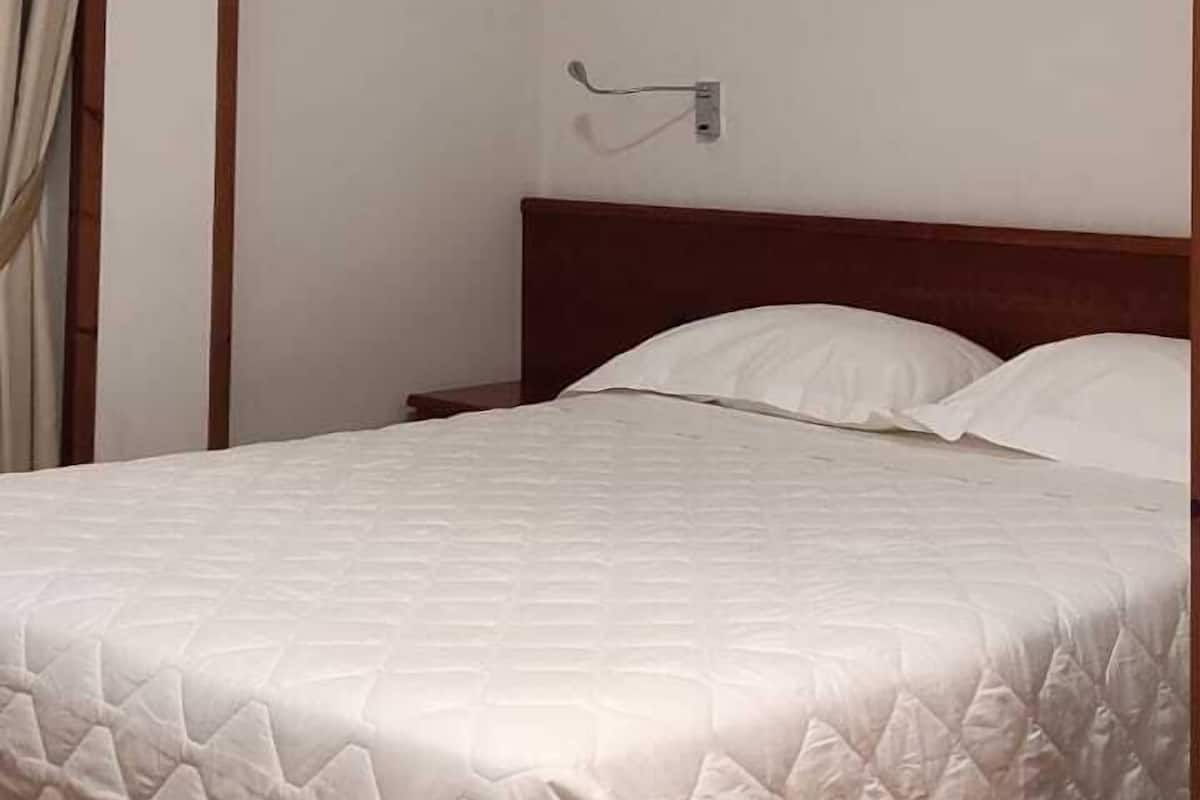 A neatly made bed with a wooden headboard, a wall-mounted light fixture, and a window with curtains.