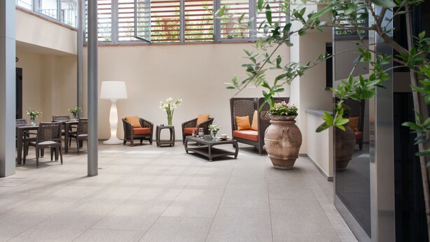 A spacious indoor area with a high ceiling, featuring a dining table set with chairs, a sofa with cushions, and a coffee table. There are large windows allowing natural light and a view of greenery outside. - Hotel La Villetta (Calenzano)