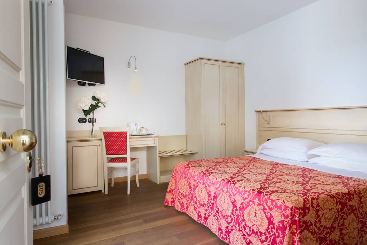 A hotel room with a bed, a desk, a chair, a wardrobe, and a TV mounted on the wall.