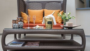 A wicker sofa with orange cushions, a glass table with a champagne bottle, a candle, and decorative items. - Hotel La Villetta (Calenzano)