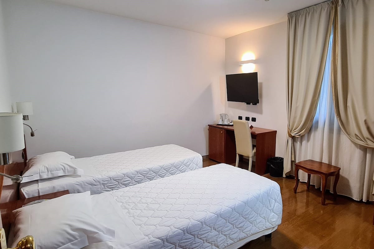 A hotel room with two beds, a desk, a chair, a television, and a wardrobe.