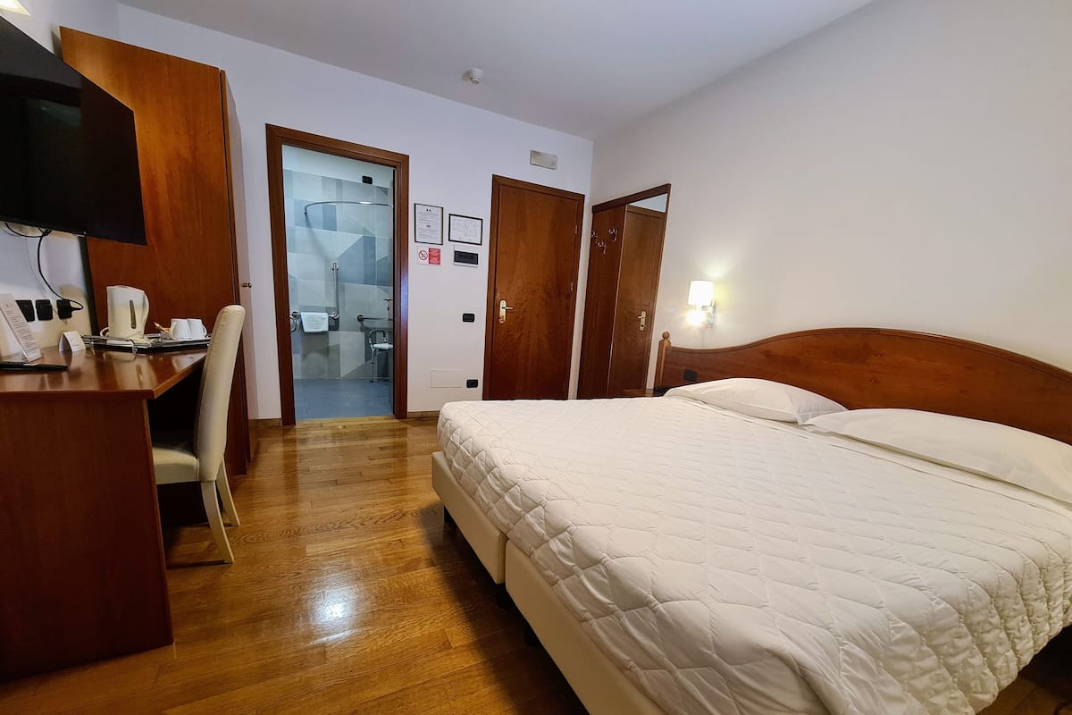 A hotel room with a wooden desk, a bed with white bedding, and a bathroom visible through an open door.