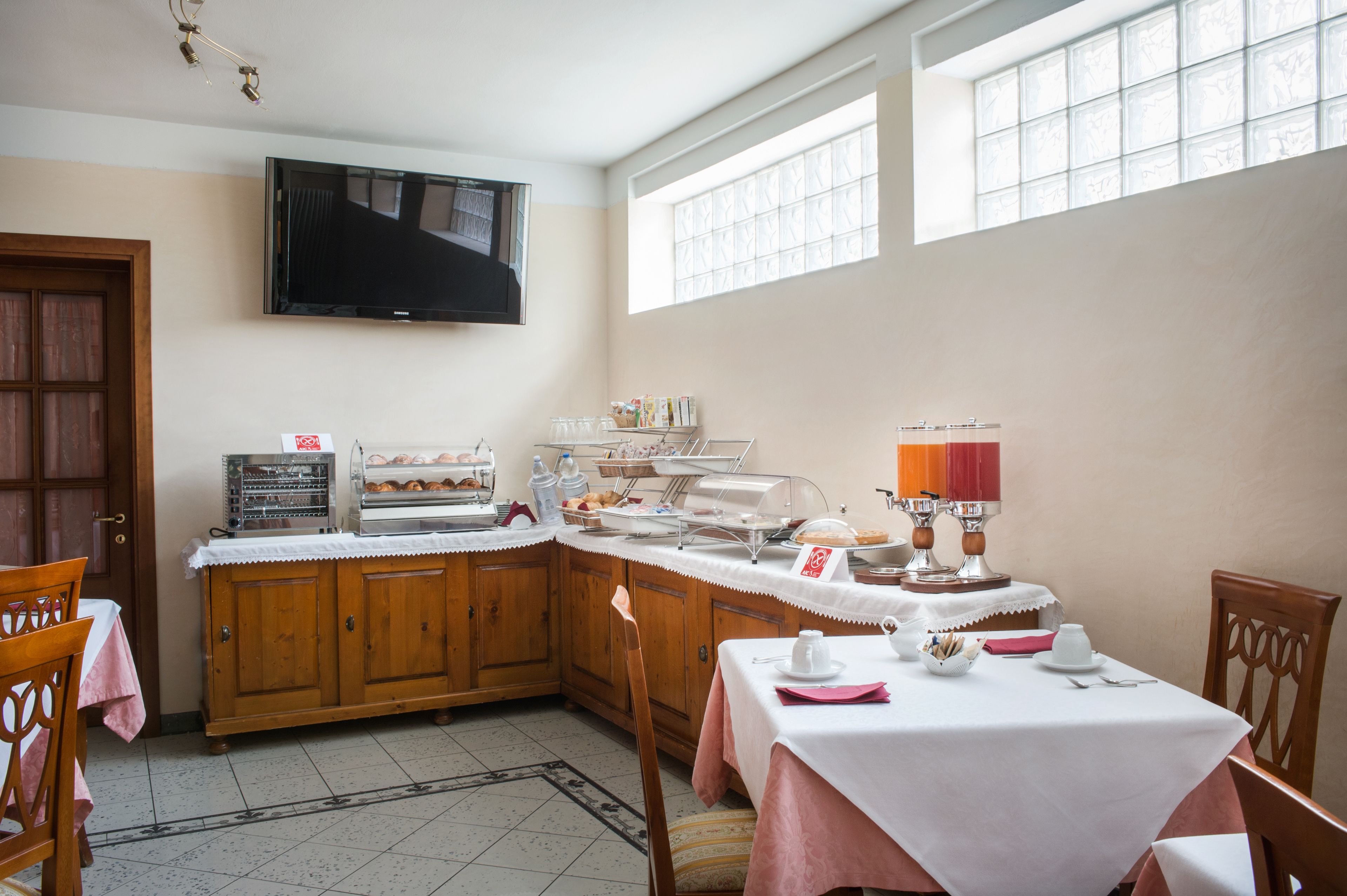 A breakfast buffet setup with a TV above, wooden cabinets, and a table with breakfast items.