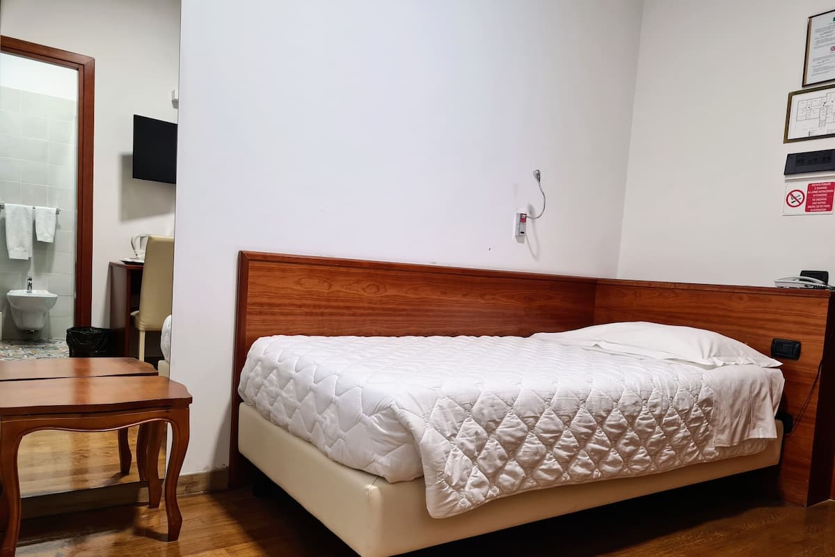 A bedroom with a wooden headboard, a white quilted bedspread, a wooden nightstand, and a small table.