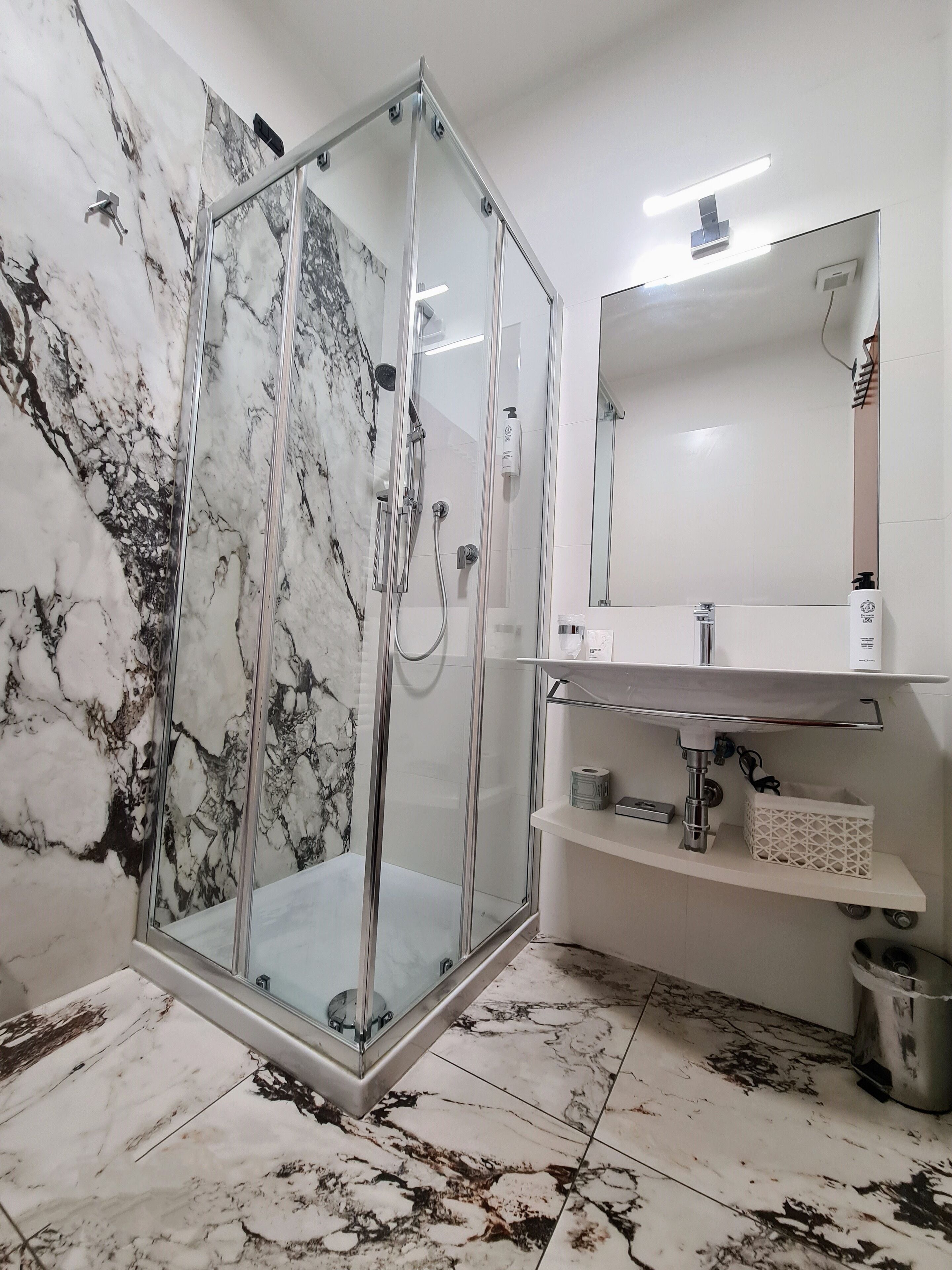 Een moderne badkamer met een douchecabine van glas, marmeren vloer en een wit wastafelmeubel met spiegel.