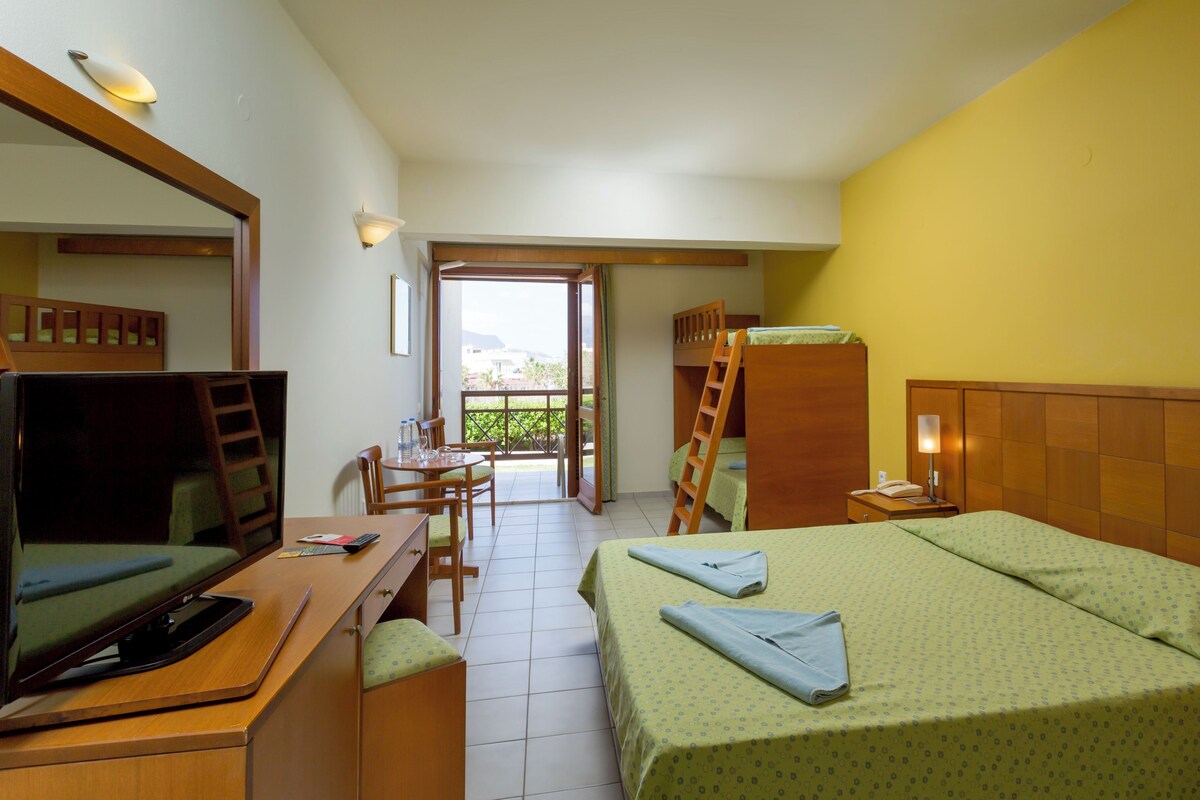Habitación de hotel con cama, escritorio con computadora, silla, escalera, mesita de noche con lámpara y vistas al exterior.