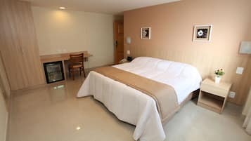 A hotel room with a bed, bedside table, chair, desk, and a small refrigerator.