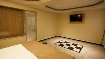 Ein Hotelzimmer mit einem Bett, einer karierten Fußmatte, einem an der Wand montierten Fernseher und einer Schiebetür.