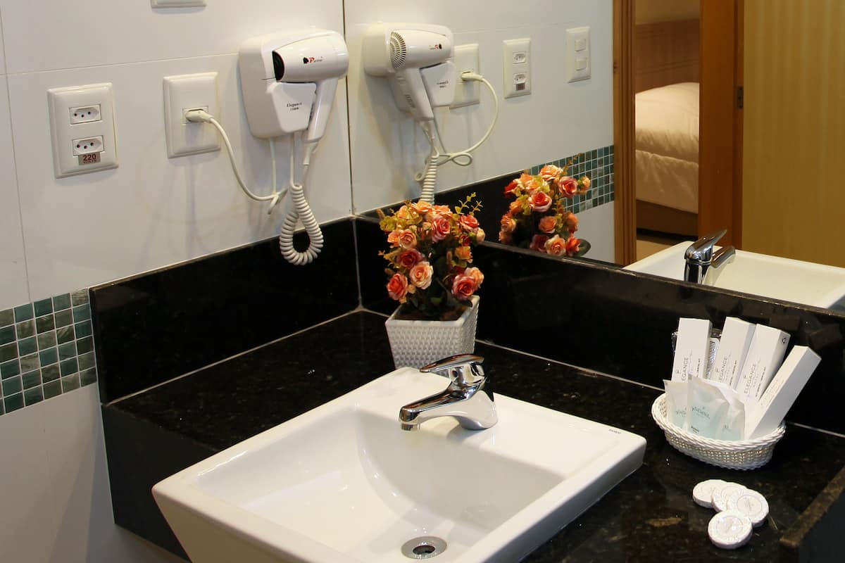 A hotel bathroom with a white sink, a hairdryer, and a basket of toiletries.