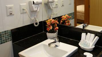 A hotel bathroom with a white sink, a hairdryer, and a basket of toiletries.