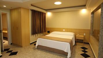 A hotel room with a large bed, a wardrobe, a bedside table, and a bathroom with a shower.